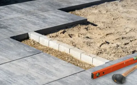 Budowa tarasu z bloczków betonowych w piasku. Poziomica i młotek czekają na dalsze prace.