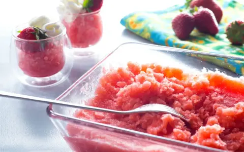 Erfrischende Erdbeer Granita in einer Glasschale, garniert mit frischen Erdbeeren und Sahne in kleinen Gläsern.