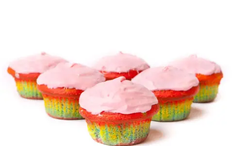 Bunte Muffins mit Lebensmittelfarbe und rosa Zuckerguss, die wie ein Regenbogen aussehen.