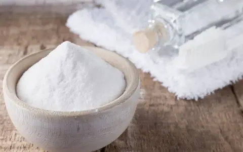 Biała soda w drewnianej miseczce, obok buteleczka z płynem i szczoteczka. Idealne do usuwania plam i jako soda na zafarbowane ubrania.
