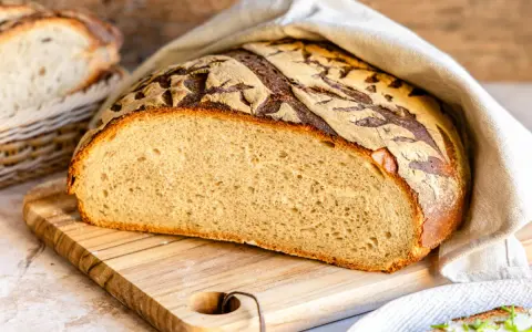 Frisches Brot mit knuspriger Kruste, bereit, mit Wasser bestrichen zu werden. Daneben ein Korb mit weiteren Brotscheiben.