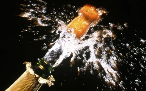Le bouchon d'une bouteille de champagne s'envole dans un jet d'eau et de bulles, un moment de joie pour sabler le champagne.