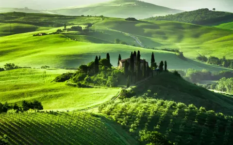 Colline verdi ondulate in Toscana, con una villa su una collina circondata da cipressi. Un sogno per un viaggio in Toscana.