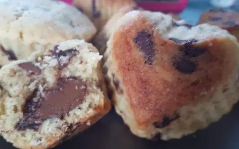 Gros plan sur des cookies moelleux en forme de cœur, débordant de pépites de chocolat. Un cookie est coupé en deux, révélant un cœur fondant.