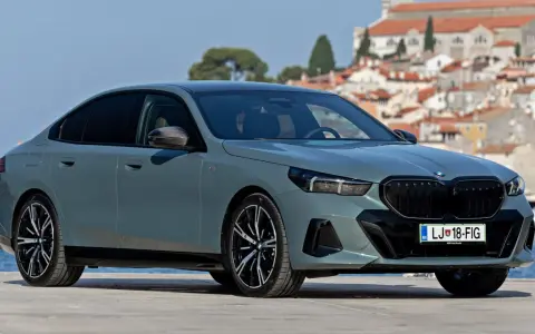 Szary BMW 520 z czarnymi felgami stoi na tle malowniczego nadmorskiego miasteczka.