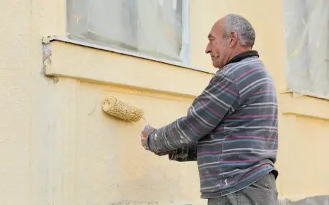 Un homme peint une façade jaune avec un rouleau.
