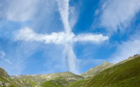 Ein Kreuz aus Wolken am blauen Himmel über grünen Bergen. Man könnte sagen, ihr werdet Zeichen am Himmel sehen.