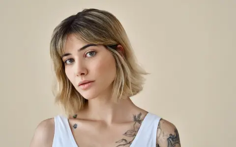 Kobieta z tatuażami na ramionach i dekolcie, z modną fryzurą long bob i grzywką.