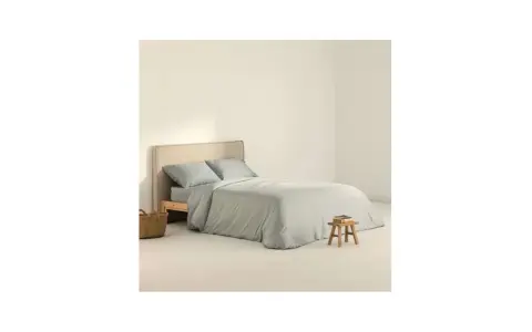 Cama con funda nordica 180x220 en tono gris claro, almohadas a juego y una cesta de mimbre al lado.