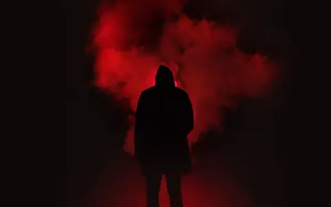 Figura incappucciata nell'oscurità, circondata da fumo rosso. Un'immagine che evoca la differenza tra giallo e noir, tra mistero e oscurità.