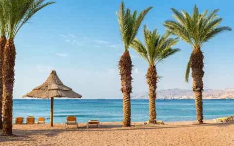 Spiaggia con palme, lettini e ombrellone di paglia. Ideale per un viaggio in Giordania, consigli per relax sul Mar Rosso.