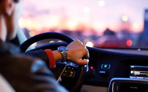 Uomo al volante, con un orologio al polso, pronto per un nuovo uber lavoro al tramonto.