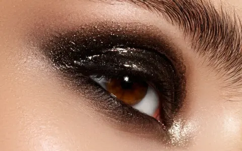 Ojo con un espectacular maquillaje ahumado marrón con brillos intensos y pestañas largas.