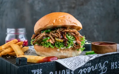 Saftiger pulled pork burger mit Salat, Jalapeños und Gurken. Die Zutaten für diesen Burger sind perfekt aufeinander abgestimmt. Dazu Pommes und Dip.