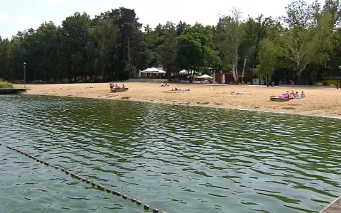 Plaża nad jeziorem Szperek, z kilkoma osobami odpoczywającymi na piasku i wodą w tle.