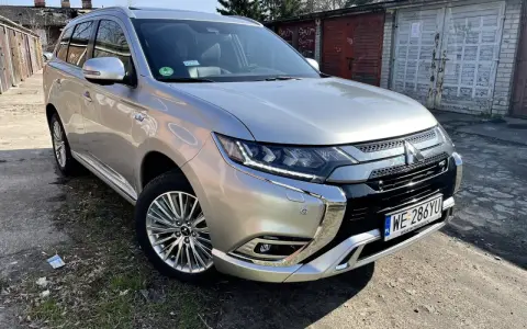 Srebrny Mitsubishi Outlander PHEV na tle garaży. Wiele osób szuka mitsubishi outlander opinie przed zakupem.
