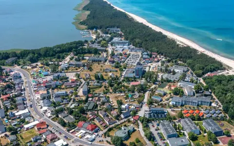 Dąbki atrakcje: widok z lotu ptaka na nadmorską miejscowość z plażą, lasem, jeziorem i zabudowaniami.