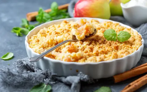 Une cuillère prélève une bouchée dorée de ce meilleur crumble aux pommes, garni de feuilles de menthe fraîche.