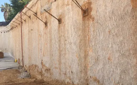 Muros pantalla de contención con anclajes metálicos, mostrando la textura rugosa de la roca y la tierra.