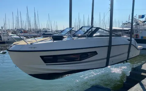 Un bateau blanc est soulevé par une grue, sa coque reflétant le soleil sur la surface mouillée du port.