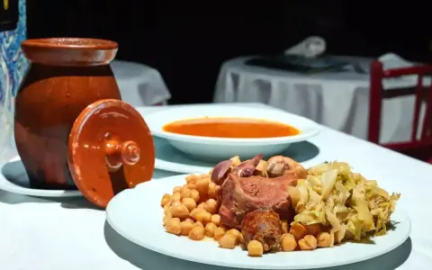 Plato de cocido madrileño con garbanzos, carne, repollo y sopa en un cuenco.