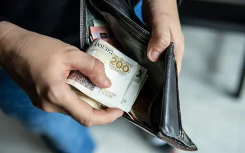 Ręce wkładają polskie banknoty 200 zł do portfela. Czy można mieć dwóch komorników na pensji, gdy pieniędzy jest tak mało?