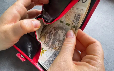 Ręce wkładają banknoty do czerwonego portfela. To może być 1000 zł na drugie dziecko, wsparcie dla rodziny.