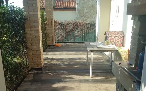 Terrazzo con pavimentazione scura, ideale per l'impermeabilizzazione. Tavolo, barbecue e vegetazione completano la scena.