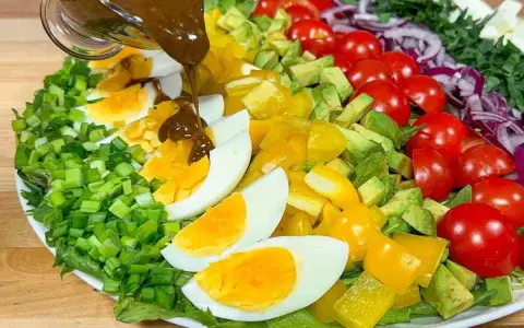 Un'insalata di avocado colorata con uova sode, pomodorini, peperoni gialli e cipolla rossa, condita con una salsa scura.