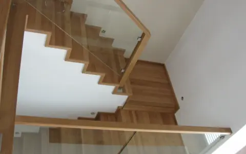 Nowoczesne schody dywanowe na beton, z drewnianymi stopniami i szklaną balustradą, tworzą lekkość i elegancję.