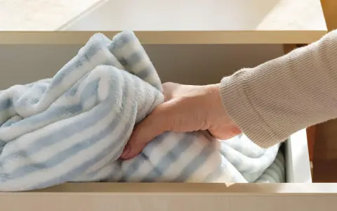 Dłoń wyjmuje z szuflady miękki, pasiasty koc. Wiesz, jak prać polar, by był jak nowy?