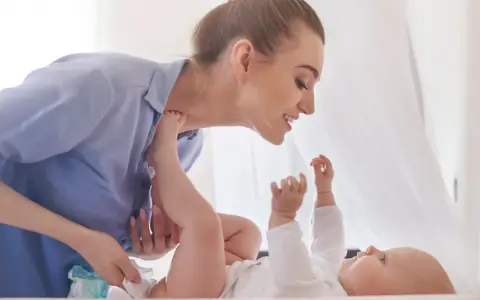 Uśmiechnięta mama zmienia pieluchę dziecku, zapewniając mu komfortowe szerokie pieluchowanie bioderek.