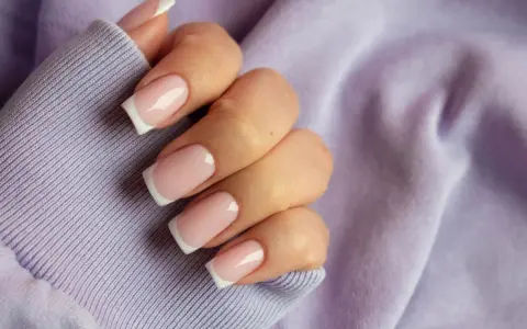 Dłoń z paznokciami w stylu french kolor, na tle lawendowej bluzy. Klasyka i elegancja.