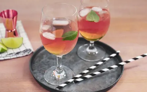 Zwei Gläser Rosato Spritz mit Eis und Minze, dazu Limettenspalten und ein Messbecher. Perfekt für einen sommerlichen Genuss.