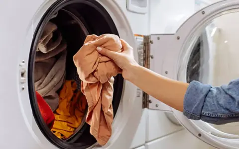 Mano saca ropa de lavadora. Es hora de limpiar lavadora a 90 grados para desinfectarla.
