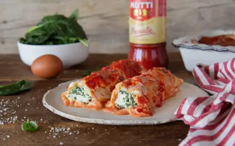 Cannelloni ricotta e spinaci fumanti, conditi con passata Mutti e formaggio filante, pronti per essere gustati.