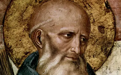 Close-up of a fresco depicting St. Benedict, with a golden halo and a wise, weathered face.