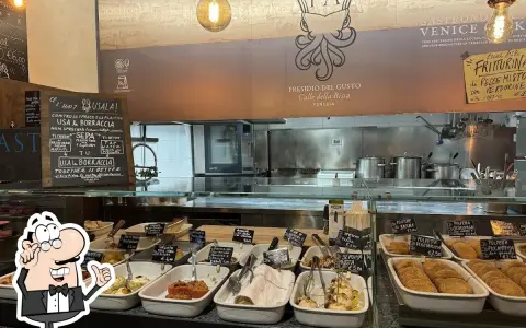 A display case filled with small dishes of food, with a chalkboard menu and a restaurant logo in the background.