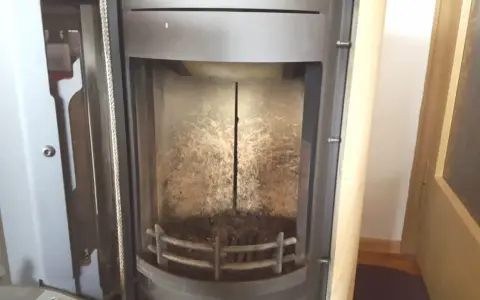 Innenraum eines Ofens mit einem vertikalen Riss im schamottstein gebrochen. Asche und Ruß bedecken den Boden und die Wände.