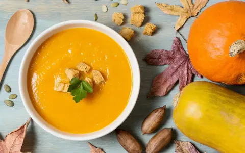 Un reconfortante tazón de puré de calabaza, adornado con picatostes y perejil, junto a calabazas, hojas de otoño y nueces.
