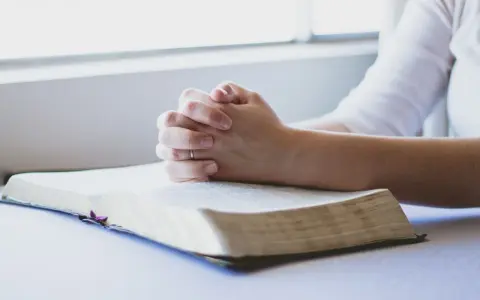 Dłonie złożone w modlitwie nad otwartą Biblią. To chwila głębokiej wiary i modlitwa o zdrowie dziecka.