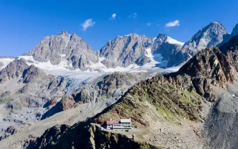 Il rifugio Marinelli, un edificio bianco e rosso, si erge su una cresta rocciosa con imponenti montagne innevate sullo sfondo.