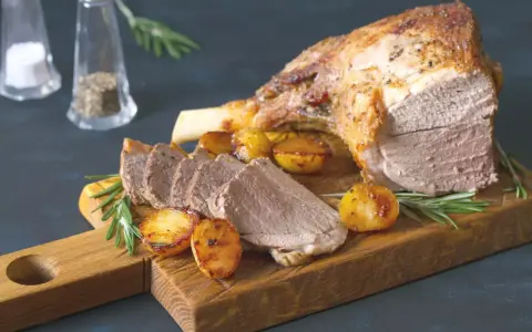 Un gigot de 7 heures, tendre et savoureux, servi avec des pommes de terre rôties et du romarin sur une planche en bois.