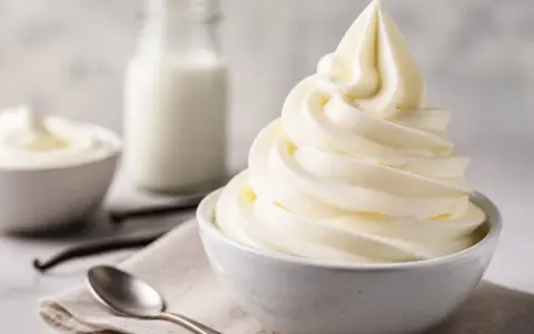 Cremiges Softeis in einer Schüssel, daneben Milch, Vanilleschoten und Löffel. Die Zutaten für das perfekte Softeis.