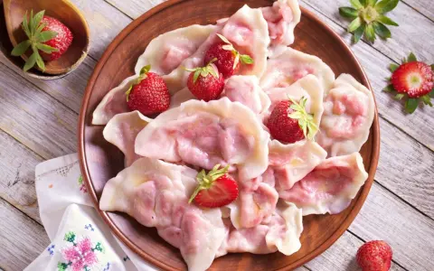 Pyszne pierogi z truskawkami, ozdobione świeżymi owocami, wyglądają apetycznie na glinianym talerzu.
