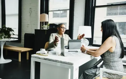 Dos mujeres discuten sobre el impuesto de sociedades y contabilidad en una oficina moderna.