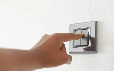 Doigt appuyant sur un interrupteur va et vient ou poussoir, sur un mur texturé.