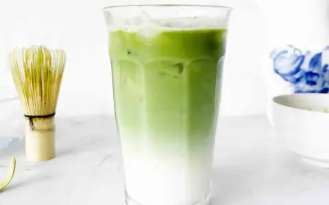 En isig matcha latte med lager av mjölk och grönt te. Bredvid står en bambuvisp, redo att blanda nästa goda dryck.
