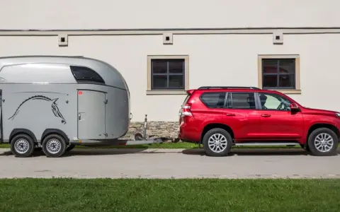 Czerwony SUV holuje przyczepę kempingową z wizerunkiem konia. Jaka kategoria na auto? To idealny zestaw do transportu zwierząt.