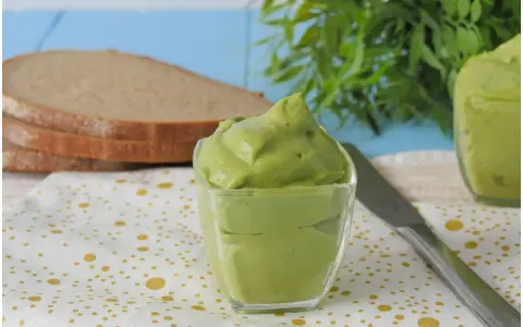 Deliziosa maionese di avocado in una ciotola di vetro, pronta per essere spalmata su fette di pane integrale.